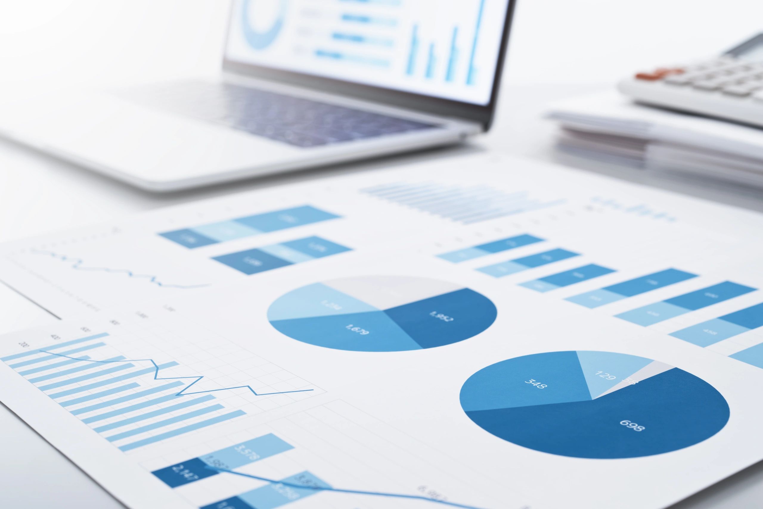 Printed financial charts in blue on a desk with a laptop and calculator.