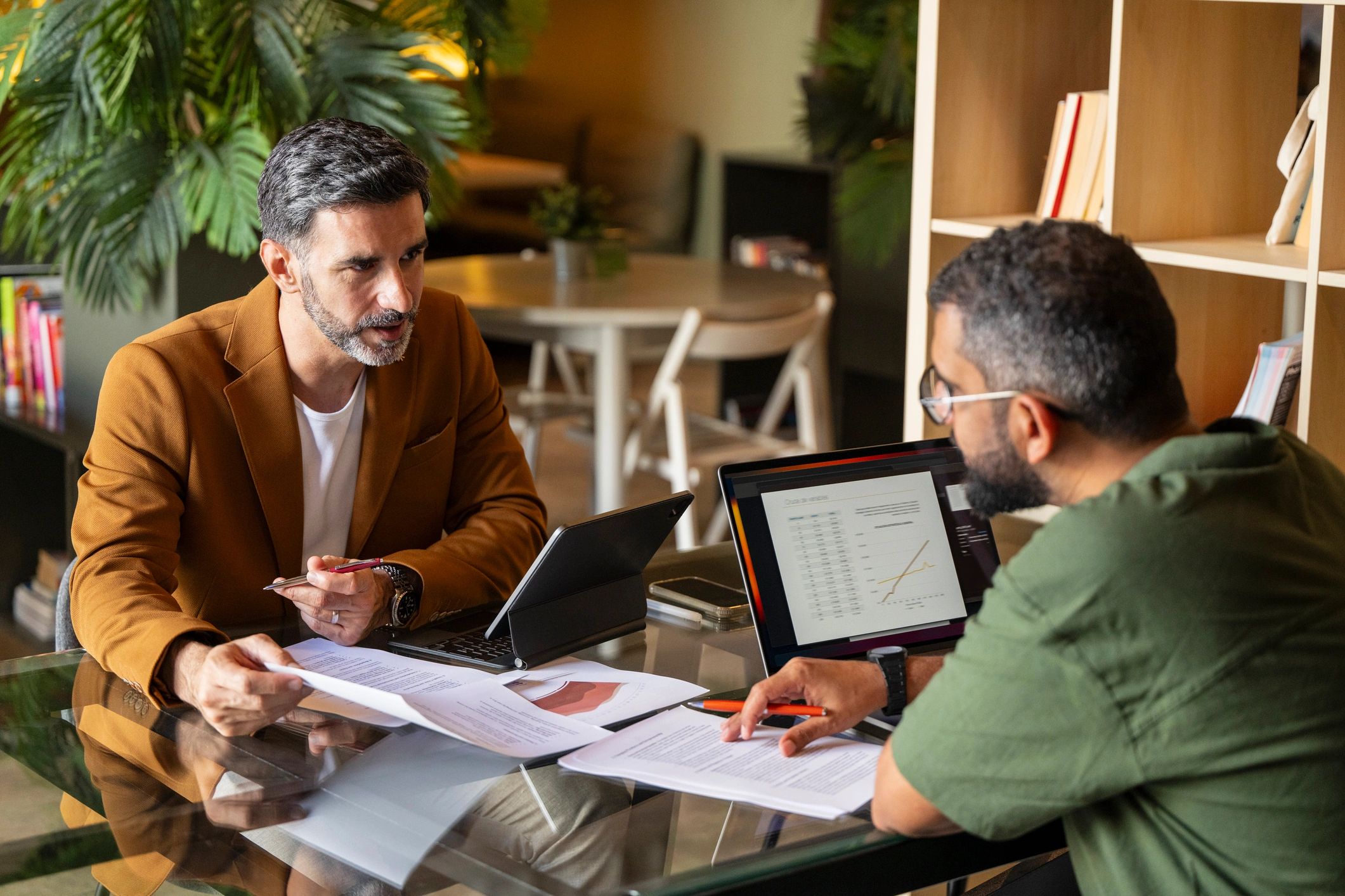 Two men discussing documents and data on laptops in a modern office.