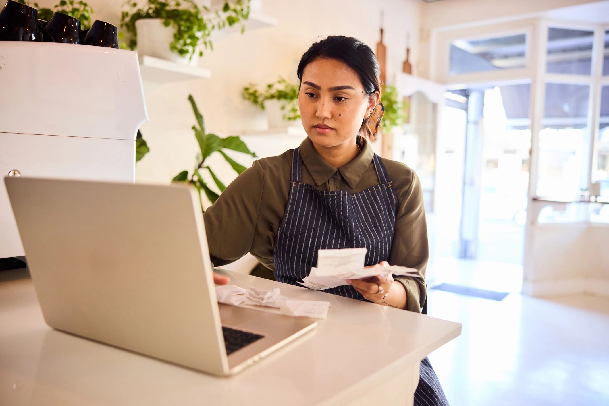 Small business owner organizing receipts while working on a laptop